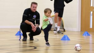 child kicking a football together with a coach from Albion in the Community