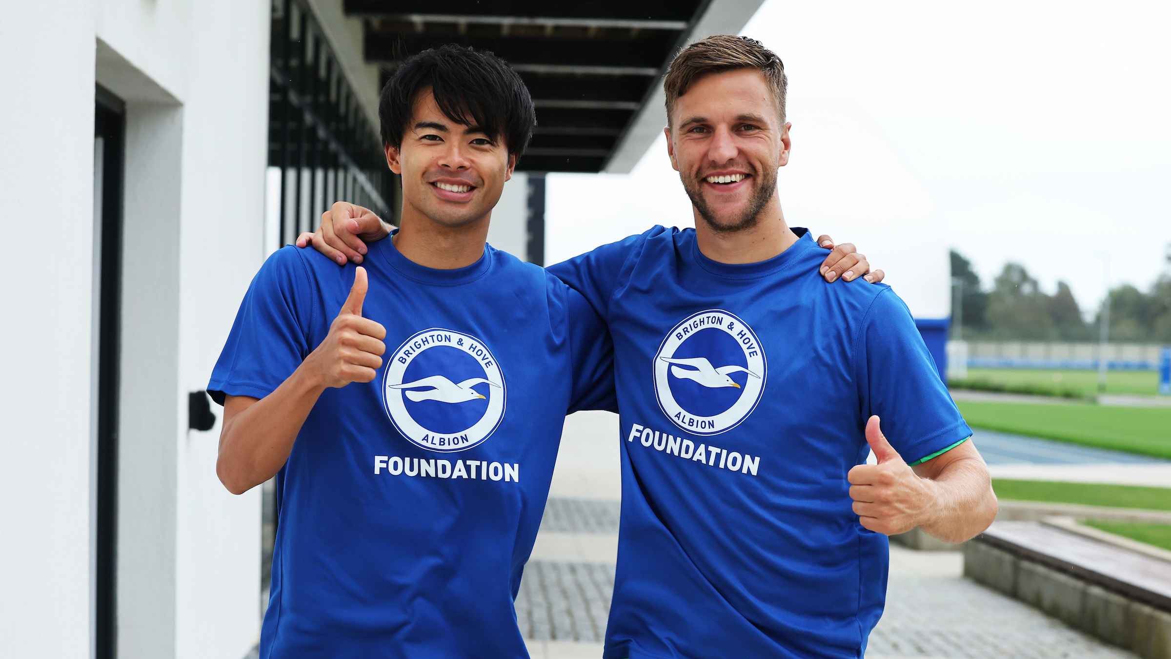 Kaoru Mitoma and Joel Veltman with their arms around each other, wearing blue BHAFC Foundation tees.