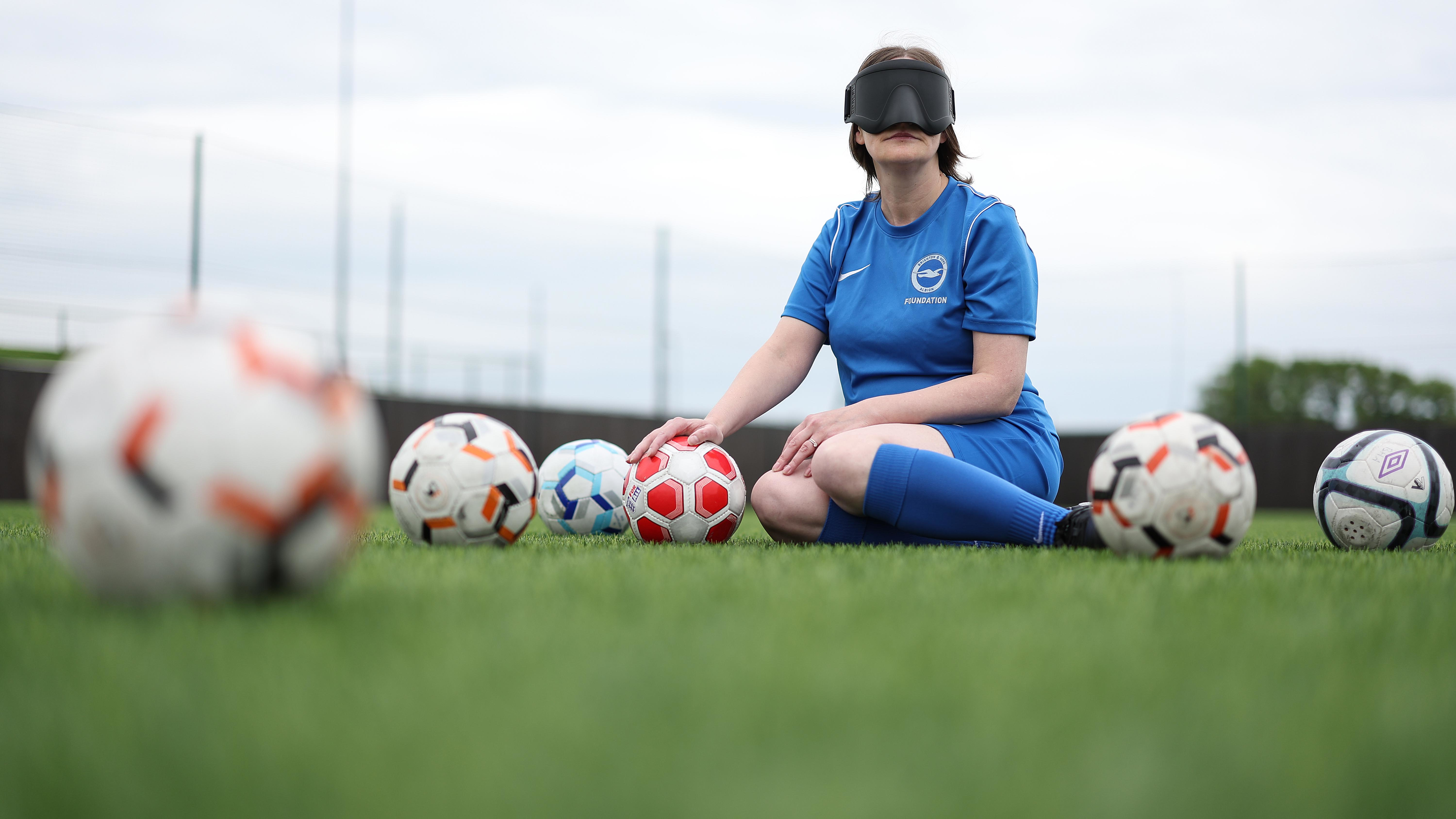 Alison sits on the floor with her eyemask on, surrounded by footballs.